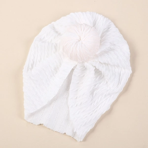 Close-up of white baby turban hat with twisted cable knit texture and top ball detail