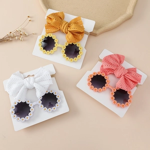 Detail view of baby daisy sunglasses and hollow lace bow headband set in soft warm colors