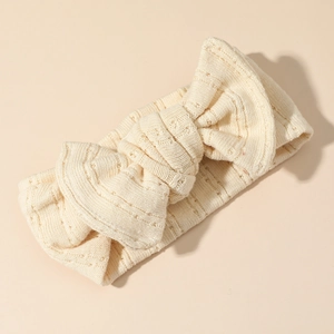 Dettaglio della maglia di cotone e del grande fiocco sulla fascia per capelli beige neonato