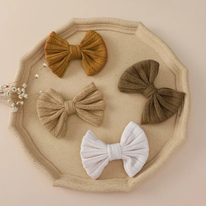 Set of four knitted bow hair clips for baby girls in earthy tones on a ceramic tray