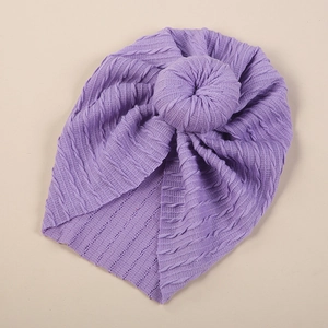 Close-up of purple knitted baby turban hat with textured braid pattern and top knot ball