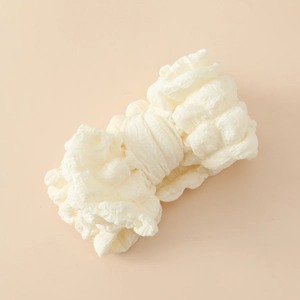 Détail de la texture gaufrée blanc crème et des plis doux sur le bandeau bébé avec nœud