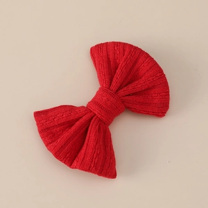 Close-up of red knitted jacquard bow hair clip with detailed ribbed texture on beige background