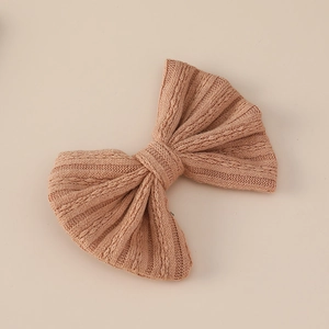 Close-up of warm brown cable knit bow hairclip with soft texture on beige backdrop