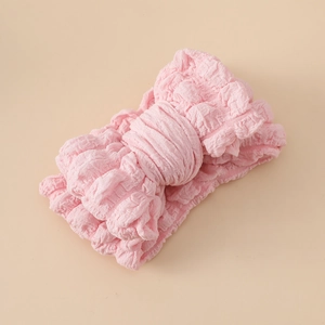 Détail d'un bandeau pour bébé avec tissu rose texturé popcorn et grand nœud élégant