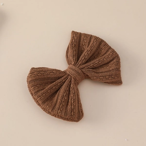 Close-up of a dark brown knitted bow hair clip with vintage cable knit texture and fabric