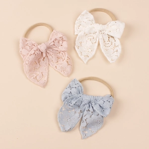 Close-up of three lace bow headbands in pink, white, and blue with soft nylon bands