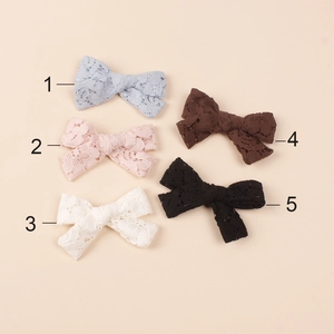 Close-up of vintage hollow lace bow hair clips in five elegant colors on a beige base
