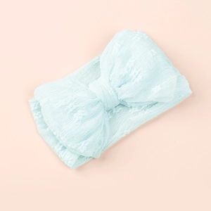 Détail d'un bandeau bébé bleu clair avec nœud en maille texturée sur fond rose doux