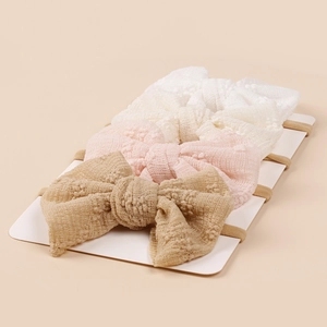 Detail of three textured baby bow headbands in white, pink, and tan on a card
