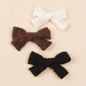 Detailed close-up of three lace bow hair clips in white, brown, and black colors