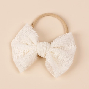Detailed view of white lace bow on a soft nude nylon headband for baby girls