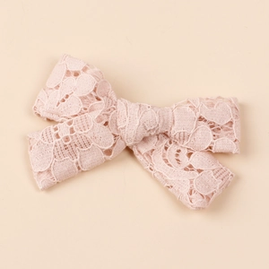 Close-up detail of a pale pink hollow lace bow hair clip with intricate floral patterns