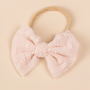 Detail view of a soft pink lace bow headband with nylon elastic for infants and toddlers