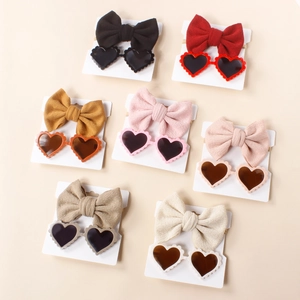 Flat lay of seven sets of newborn knit bow headbands with matching heart-shaped sunglasses