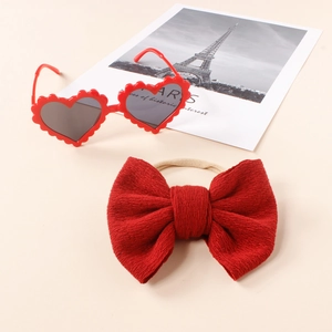 Kids red heart sunglasses and matching knit bow headband set displayed on a beige background