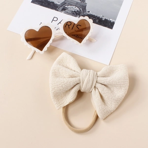 Flat lay of cream ribbed bow headband and white heart-shaped sunglasses for babies