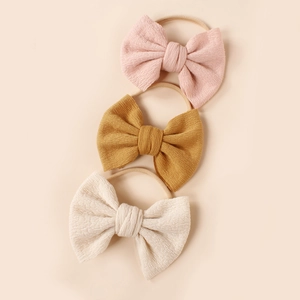 Detailed view of three textured fabric bow headbands in pink, yellow and beige colors