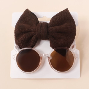 Detail of pink bear-ear sunglasses and brown knit bow headband on white card