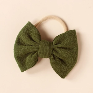 Close-up of a dark green ribbed knit bow on a soft nude nylon headband for infants