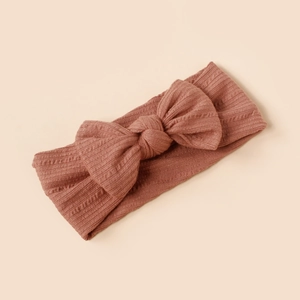 Detail of baby headband featuring soft ribbed fabric and large bow in dusty rose