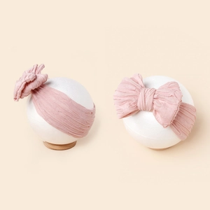 Détail d'un bandeau bébé rose clair avec doubles nœuds sur tricot élastique