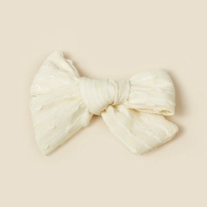 Vue détaillée montrant la texture tissée crème et le nœud en tissu sur la pince à cheveux