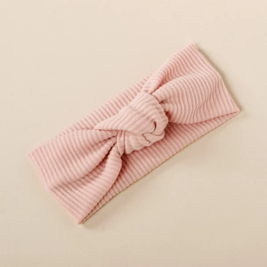 Detail of pink ribbed knit baby headband with elastic knot design on beige background