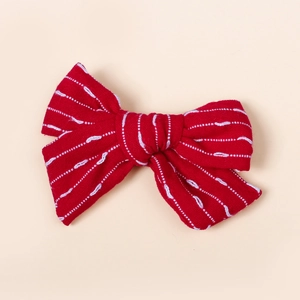 Détail d'une pince à cheveux avec nœud rouge fait main et broderie blanche ondulée