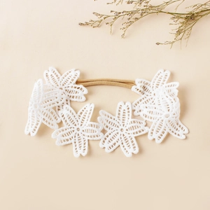 Détail de fleurs en dentelle blanche brodée sur un bandeau souple pour bébé fille