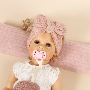 Realistic baby doll with blue eyes wearing a pink lace bow headband and lace dress