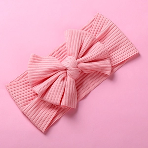 Close-up of baby headband with ribbed texture and large bow in soft pink fabric