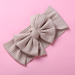 Close-up of baby ribbed knit headband with large 3D bow in light beige on pink background