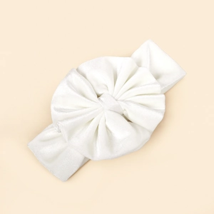 Détail d'un bandeau blanc en velours pour bébé montrant la texture plissée et le grand nœud