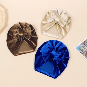 Flat lay of velvet baby turban hats in brown, beige and royal blue with large bows