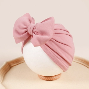 Detail view of pink baby turban hat featuring a large bow and soft pleated knit texture