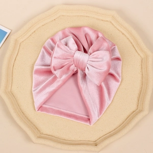 Detail of pink velvet baby turban with a large bow and soft pleated texture on a tray