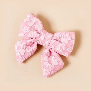 Dettaglio di un fermaglio per capelli a fiocco rosa con trama jacquard e stile dolce