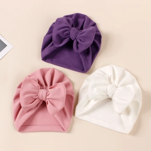 Detailed view of three soft knit baby turbans in purple, pink and white with big bows