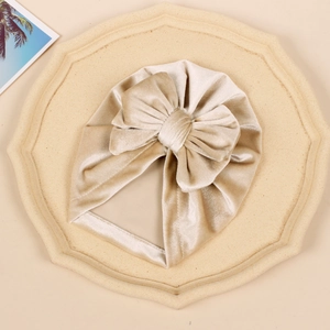 Detailed view of champagne velvet baby turban hat with a large bow on a display tray