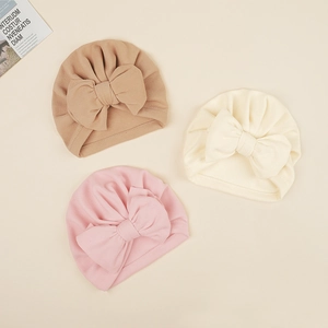 Three soft knit baby turbans with oversized bows in brown, beige, and pink colors