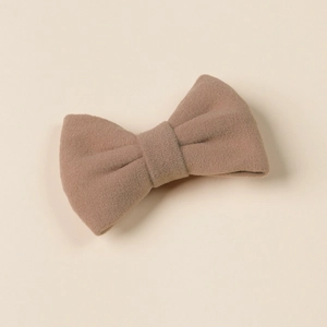 Close-up of a warm camel cashmere texture bow hair clip for girls on a soft beige base