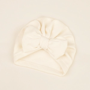 Macro detail of soft knit cream infant turban hat with a large 3D decorative bow