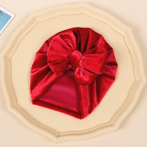 Detail of red baby velvet turban hat with oversized bow on a minimalist stone tray