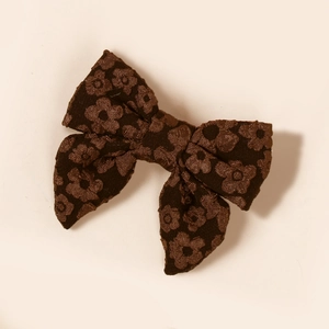 Dettaglio del fermaglio a fiocco in tessuto jacquard marrone scuro con fiori per bimba
