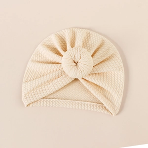 Close-up of cream waffle-knit baby turban hat with a stylish donut knot detail