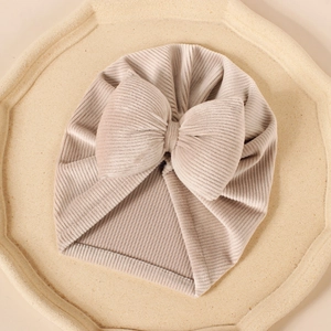 Gros plan du turban pour bébé en velours beige avec grand nœud sur plateau texturé