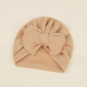 Detail of soft beige baby turban hat featuring a large decorative bow and pleated knit