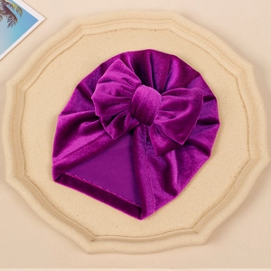 Detailed close-up of a purple velvet baby turban hat with a large golden bow decoration