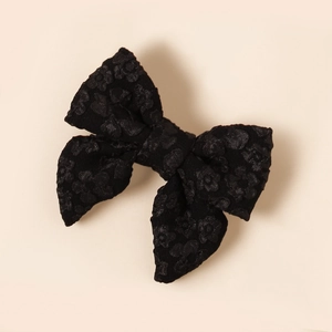 Dettaglio del fermaglio per capelli a fiocco in tessuto jacquard nero su sfondo beige chiaro